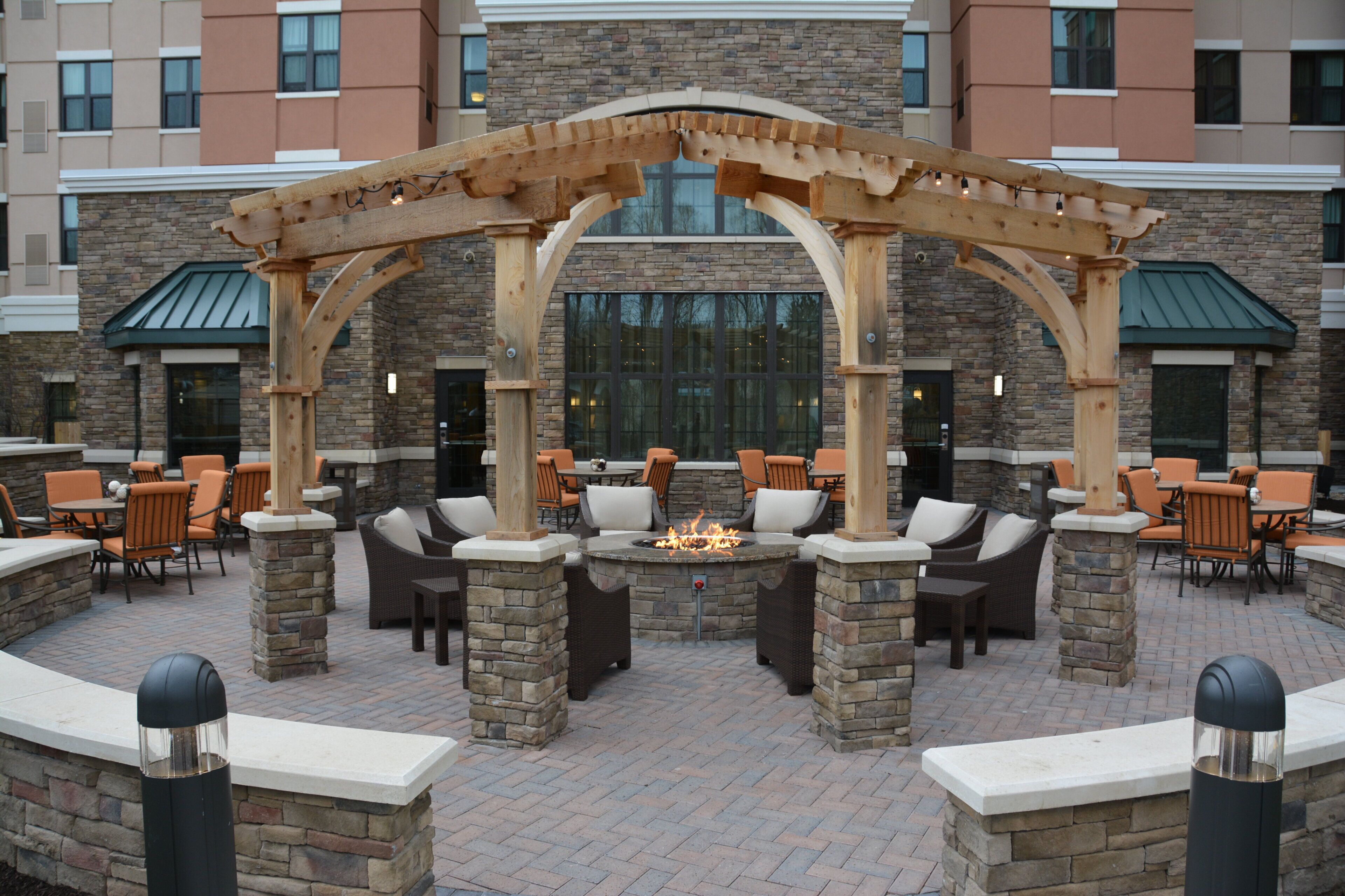 An outdoor patio area with stone pillars, wooden pergola, and seating arrangements.