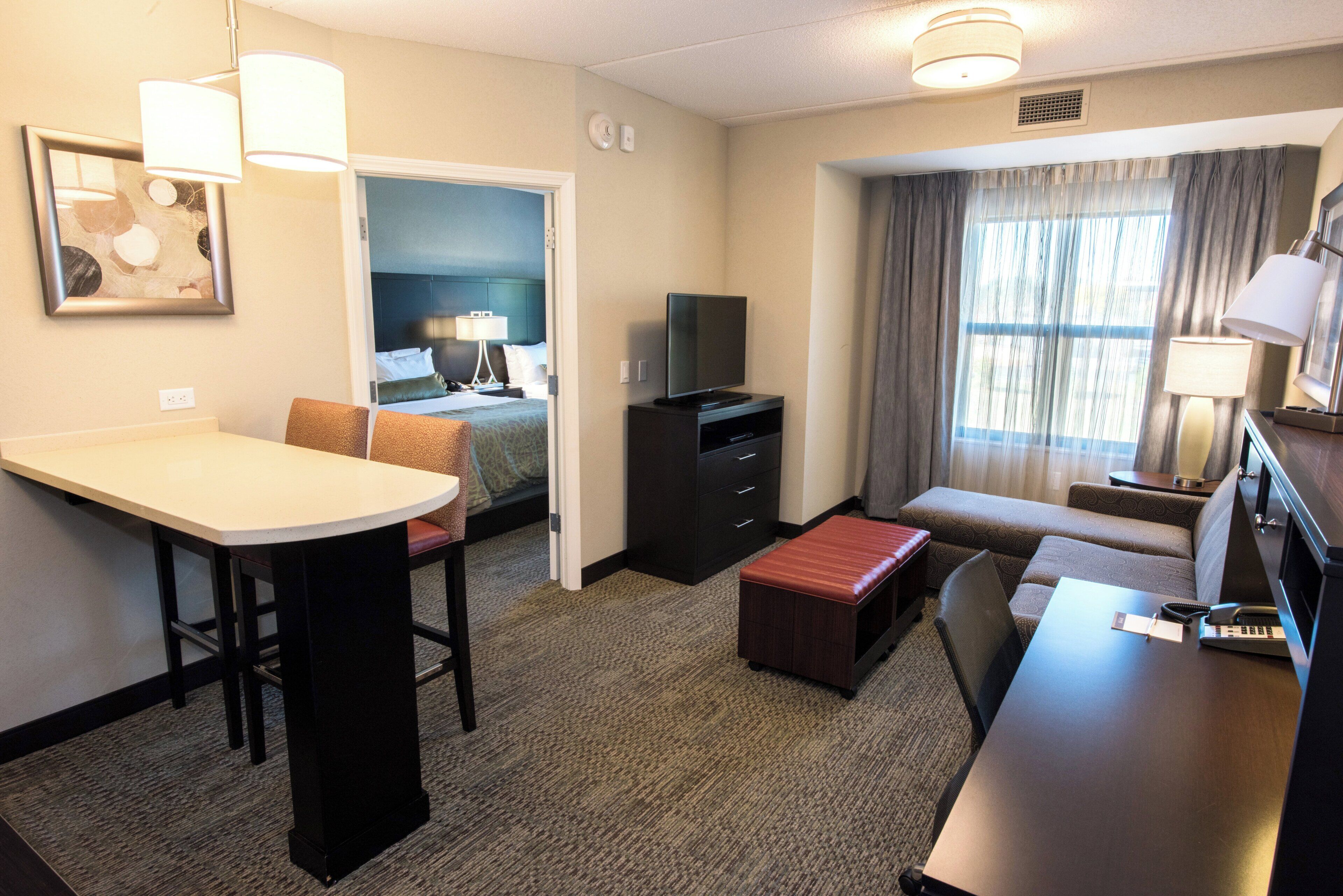 A hotel room with a bed, a desk, a television, a sofa, and a window with curtains.