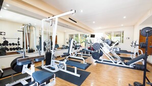 Un gimnasio con diversos equipos de ejercicio, espejos y suelo de madera.