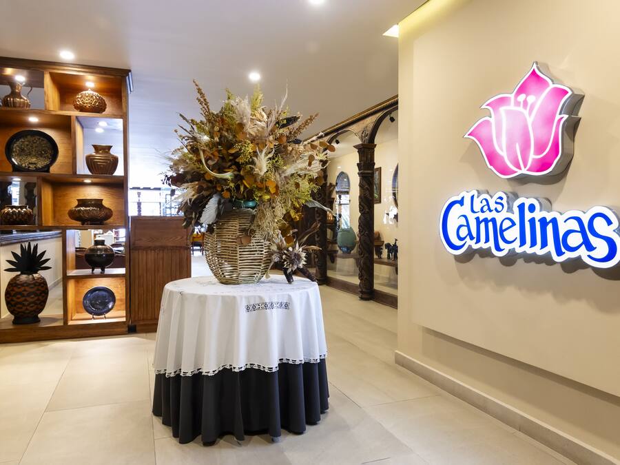 A reception area with a floral centerpiece on a table, a wooden display of pottery, and a neon sign reading "Las Camelinas".