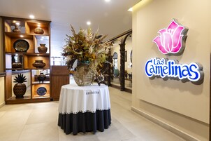 Un área de recepción con un centro de mesa floral sobre una mesa, una exhibición de cerámica en madera y un letrero de neón que dice "Las Camelinas".