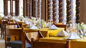 Un restaurante con manteles amarillos y sillas de madera, que cuenta con una larga zona de comedor y altos pilares de madera.