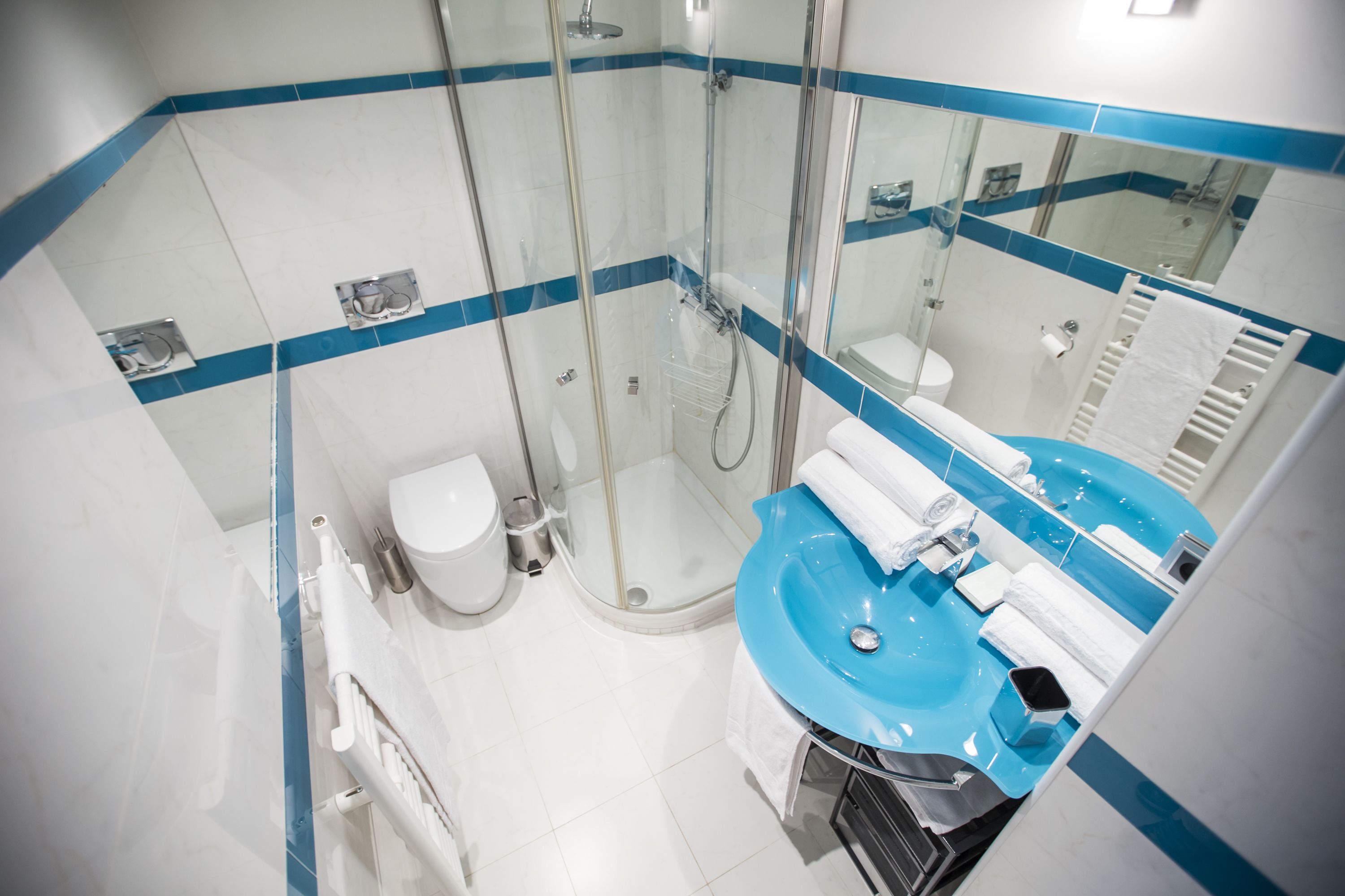 Un bagno moderno con doccia vetrata, un water bianco e un lavandino blu con uno specchio sopra.