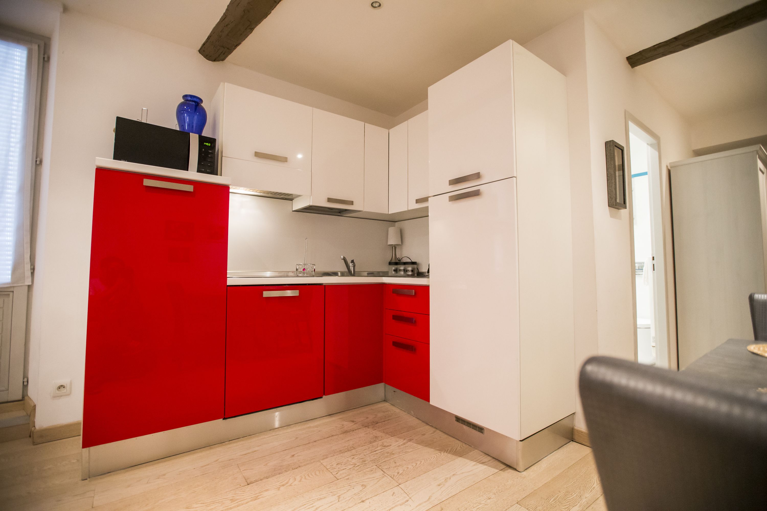 Una cocina moderna con armarios blancos y rojos, un microondas y un lavamanos.