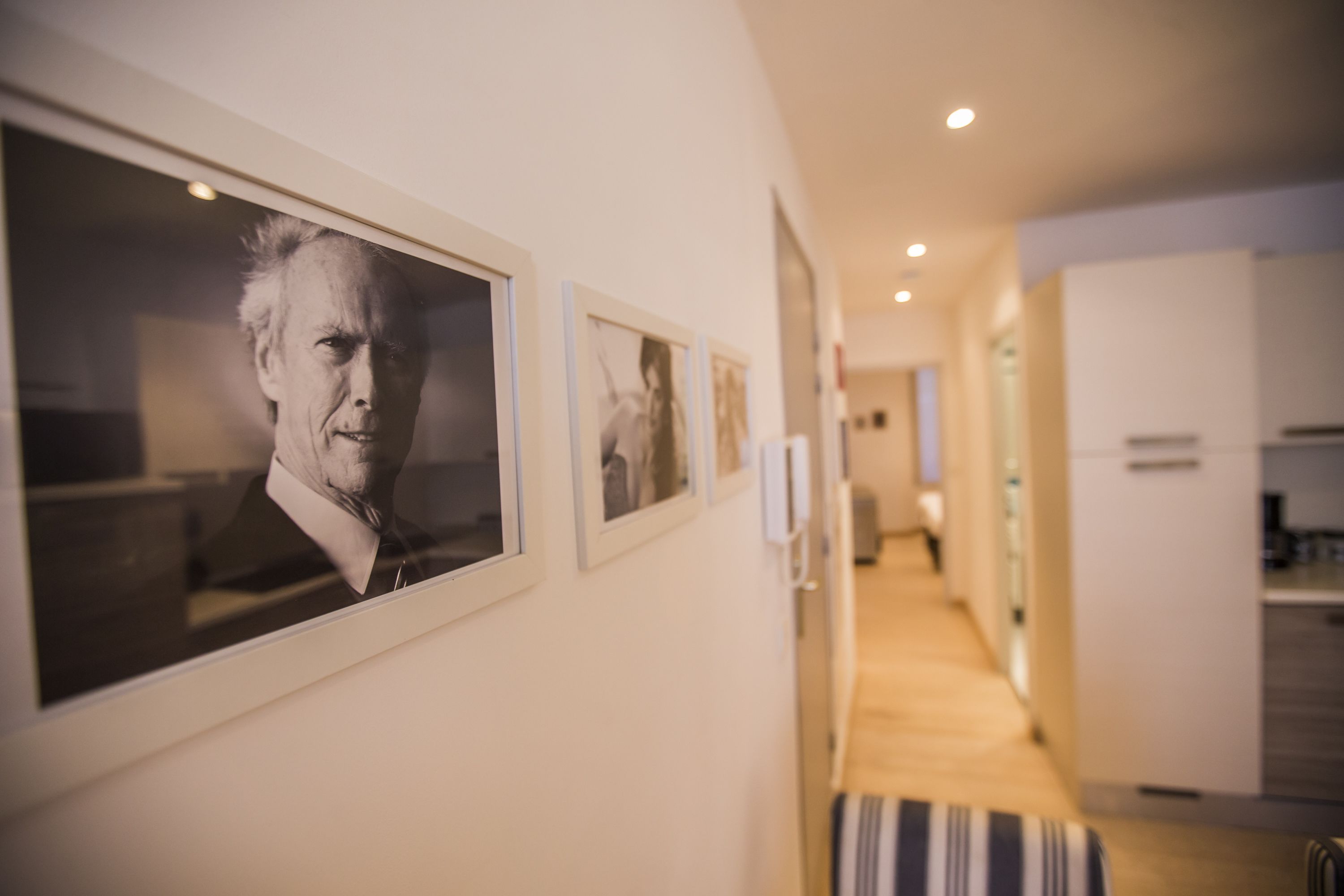 Ein Flur mit gerahmten Porträts an der Wand, einer gestreiften Bank und einem Küchenbereich im Hintergrund.