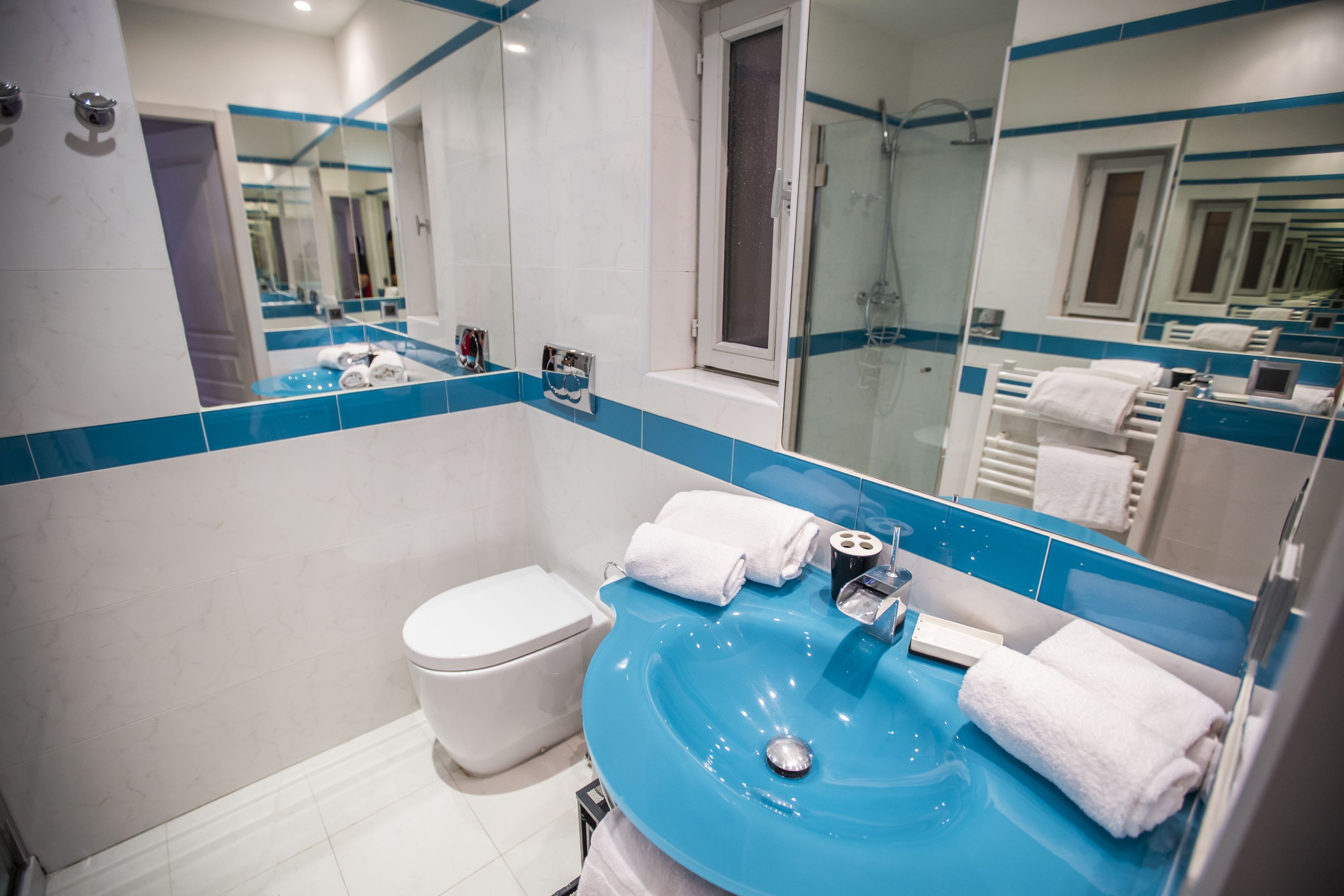 Un baño moderno con un lavamanos azul, inodoro blanco y un espejo grande.