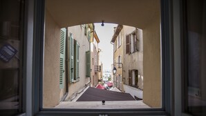 A narrow street with buildings on either side, viewed through a window with a metal frame. - Residence Bouttau (Cannes)