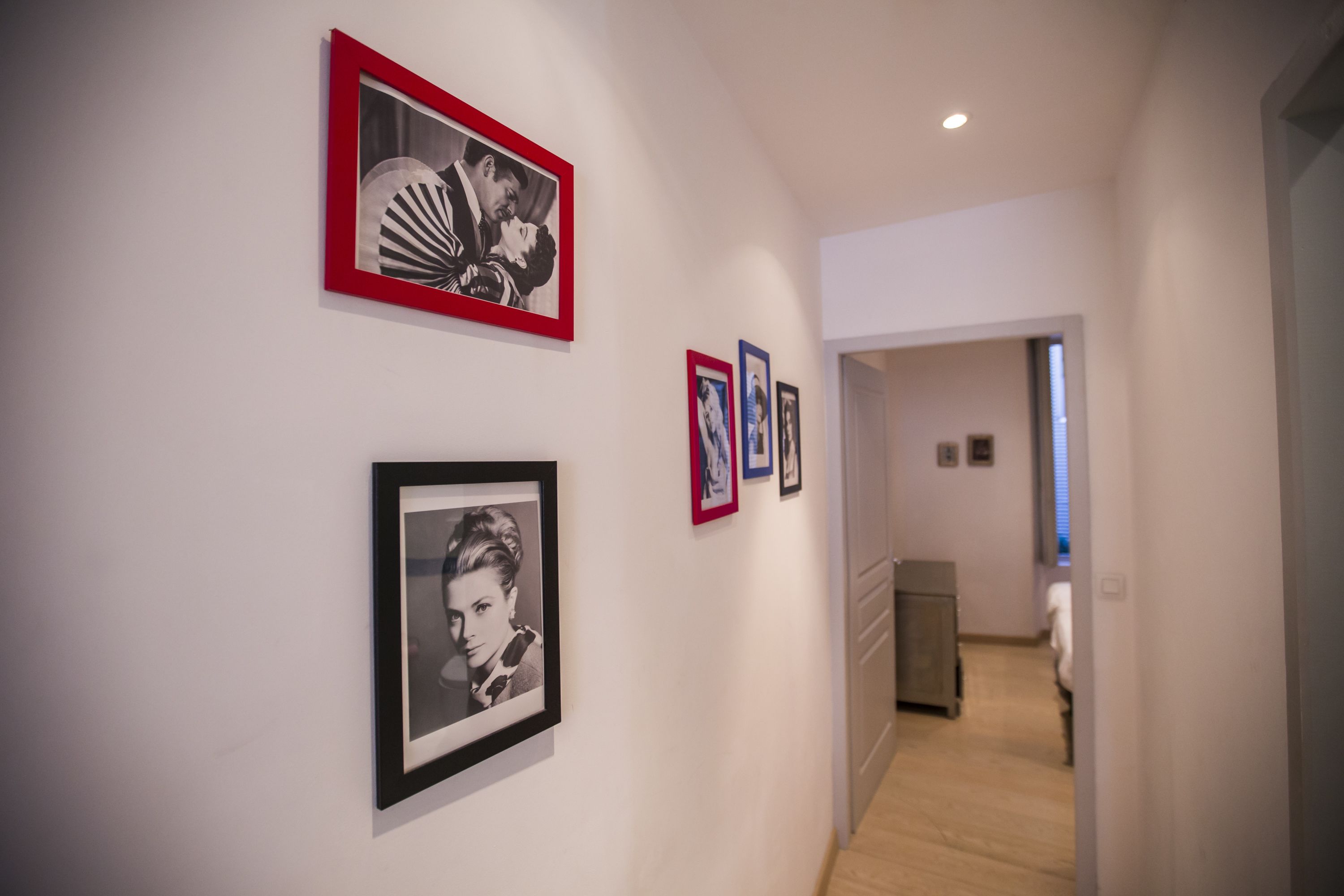 A hallway with framed pictures on the wall, a door at the end, and a light fixture on the ceiling.