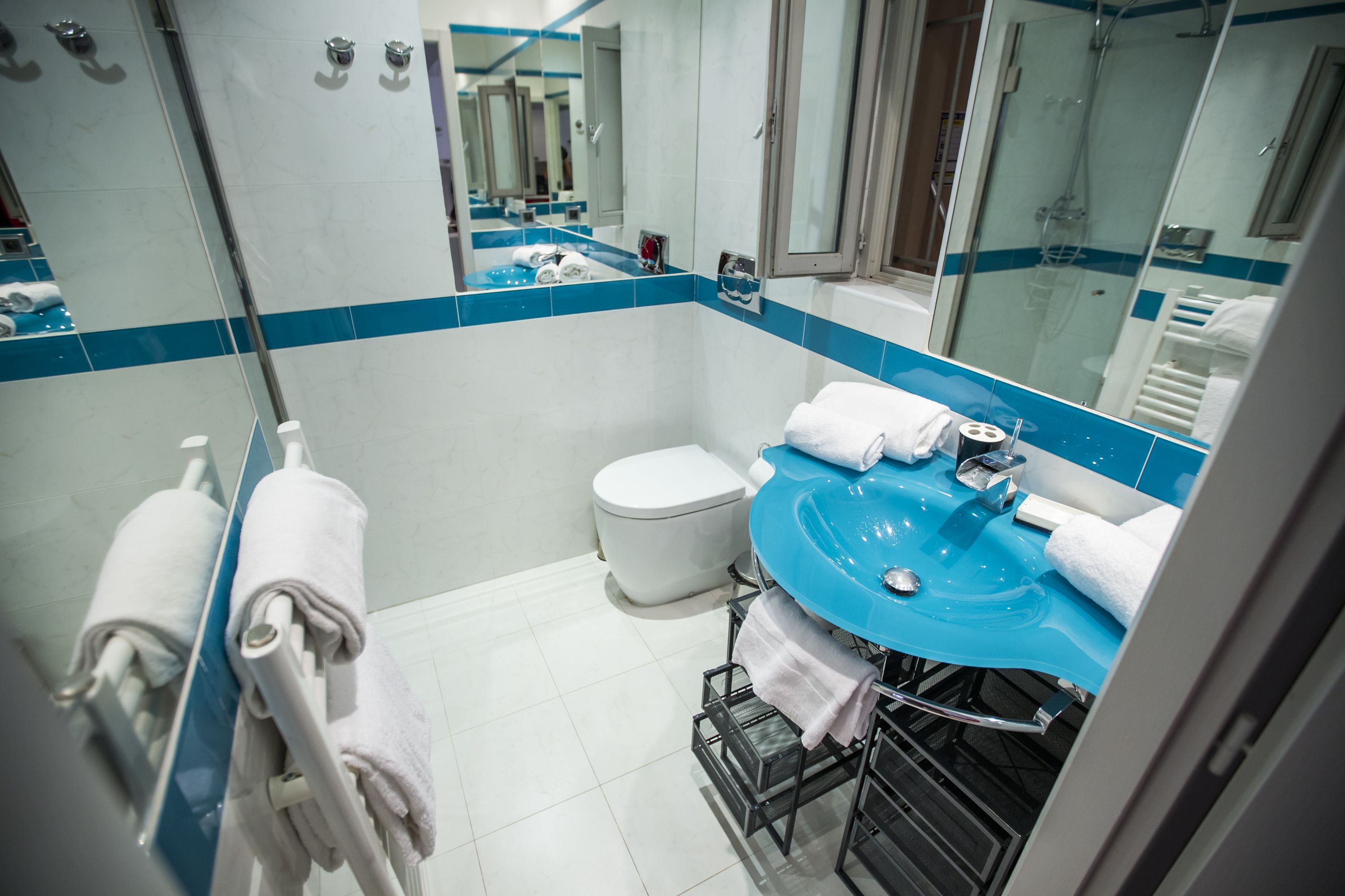 Un baño moderno con lavamanos de azulejos azules, inodoro blanco y ducha con cerramiento de vidrio.