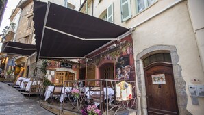 An outdoor café with tables and chairs, a wooden door, and a signboard. - Residence Bouttau (Cannes)