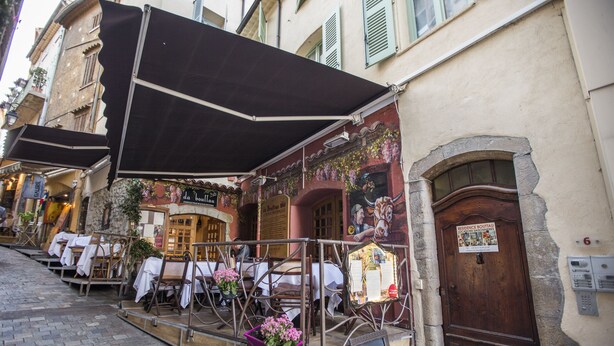 An outdoor café with tables and chairs, a wooden door, and a signboard. - Residence Bouttau (Cannes)
