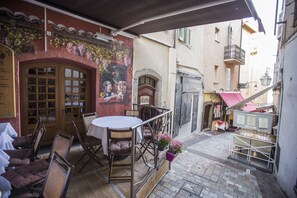 Un café en plein air avec des tables et des chaises, une fresque murale et une petite boutique en arrière-plan.