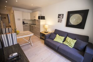 Un salon moderne avec un canapé, une table basse et un téléviseur. Il y a également un coin cuisine équipé de placards et d’un four à micro-ondes.