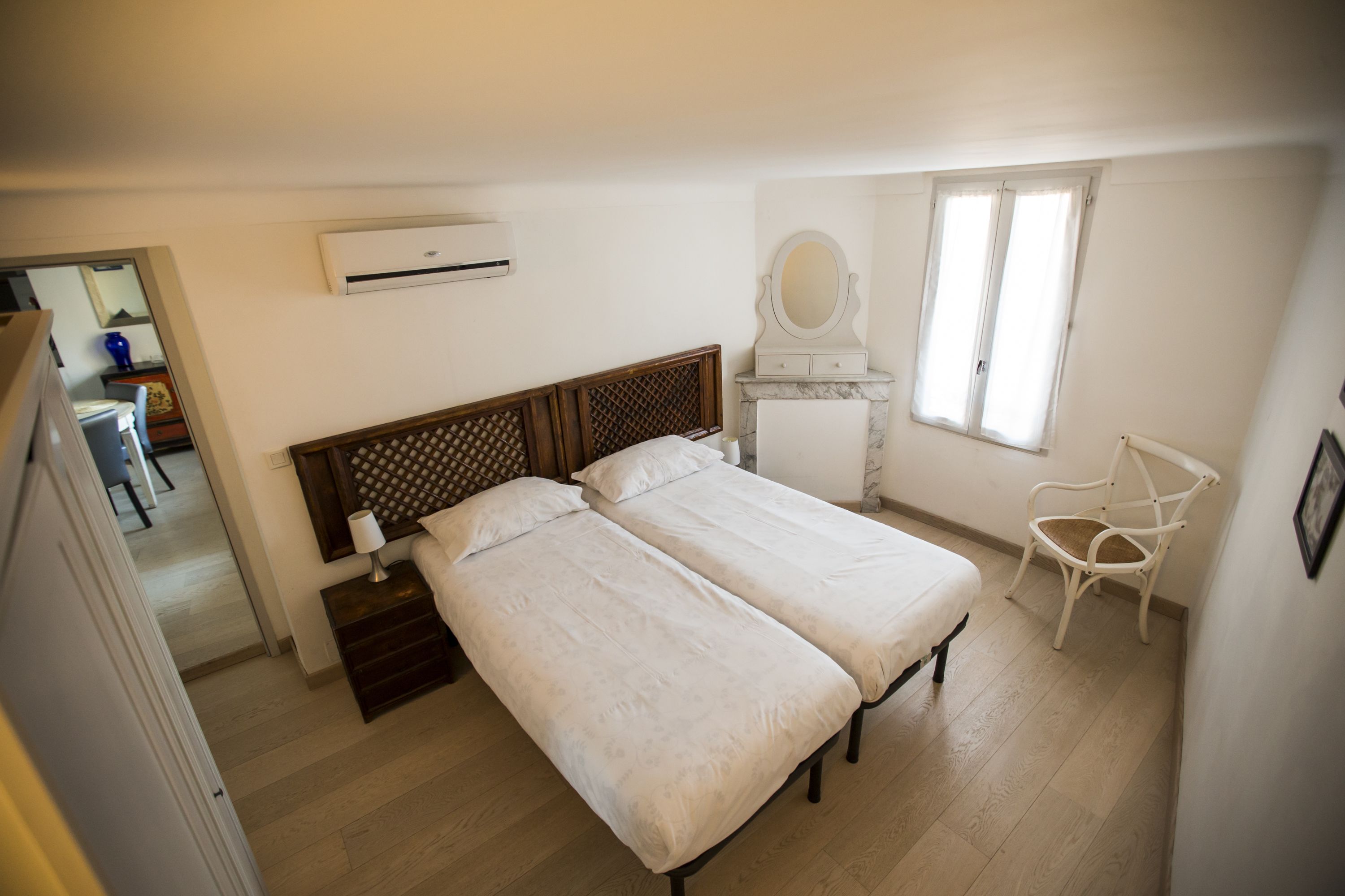 Ein Schlafzimmer mit zwei Betten, einem Sessel, einem Spiegel und einer Klimaanlage.