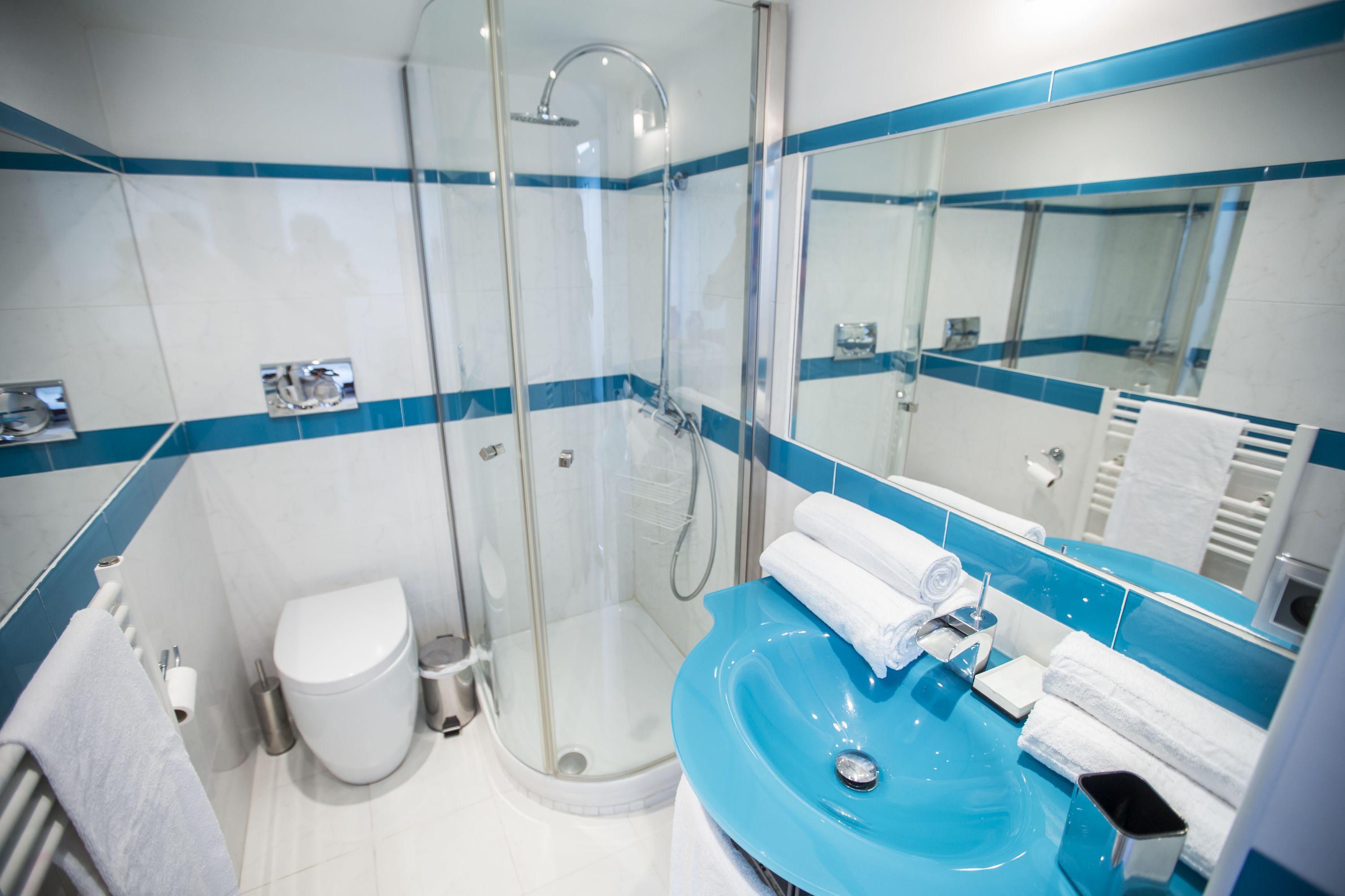 A modern bathroom with a glass-enclosed shower, a white toilet, a blue sink, and a large mirror.