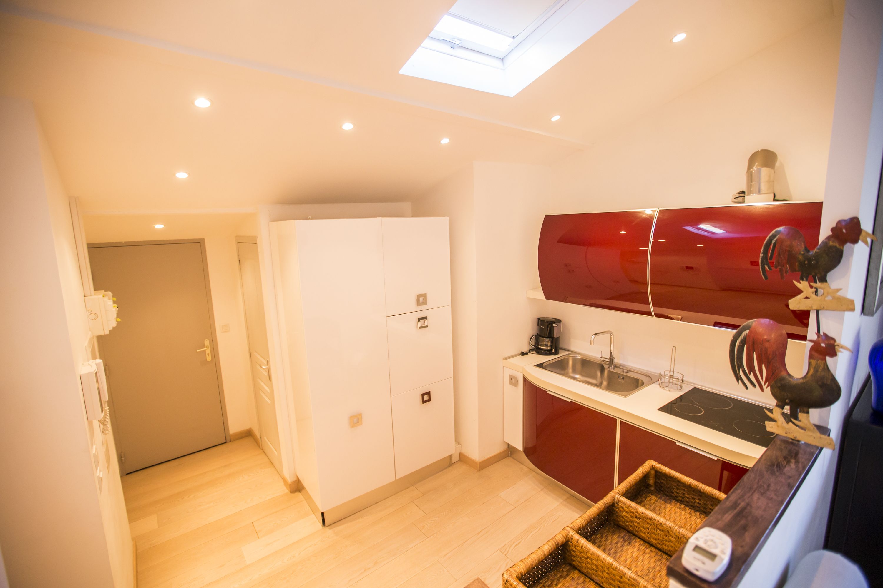 A compact kitchen with a skylight, a red refrigerator, and a rooster decoration.