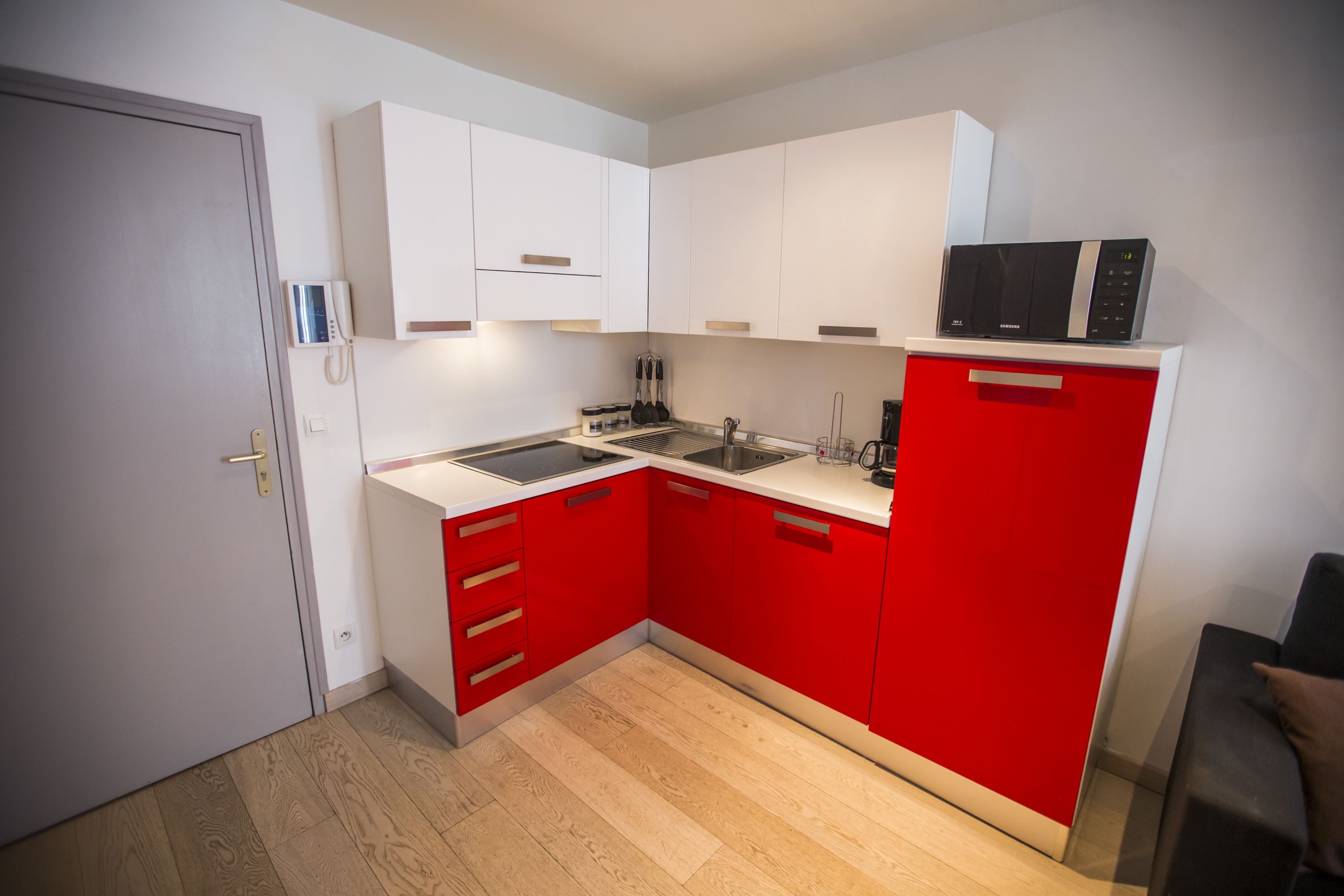 A compact kitchen with white upper cabinets, red lower cabinets, a microwave, and a sink.