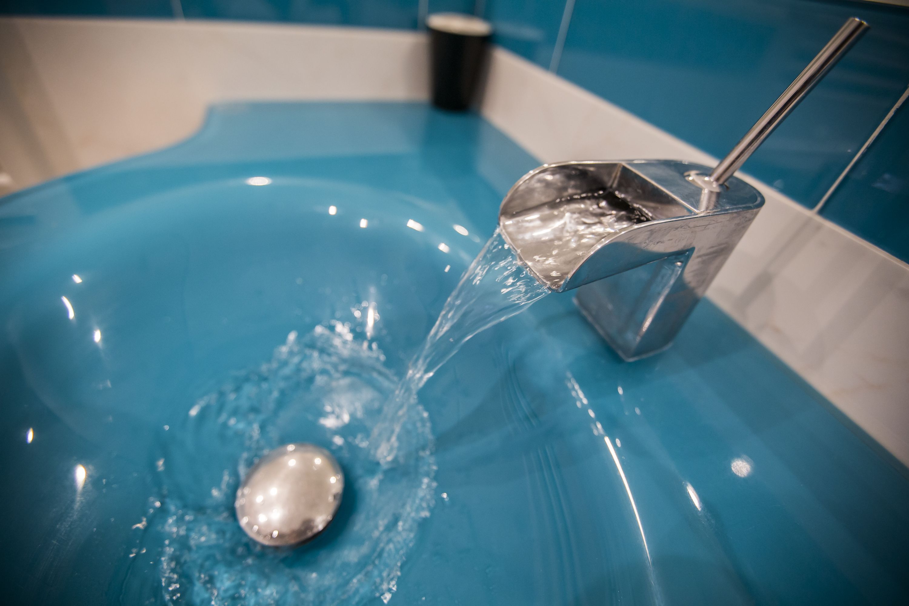 A blue bathtub with a handheld showerhead and a cup in the background.