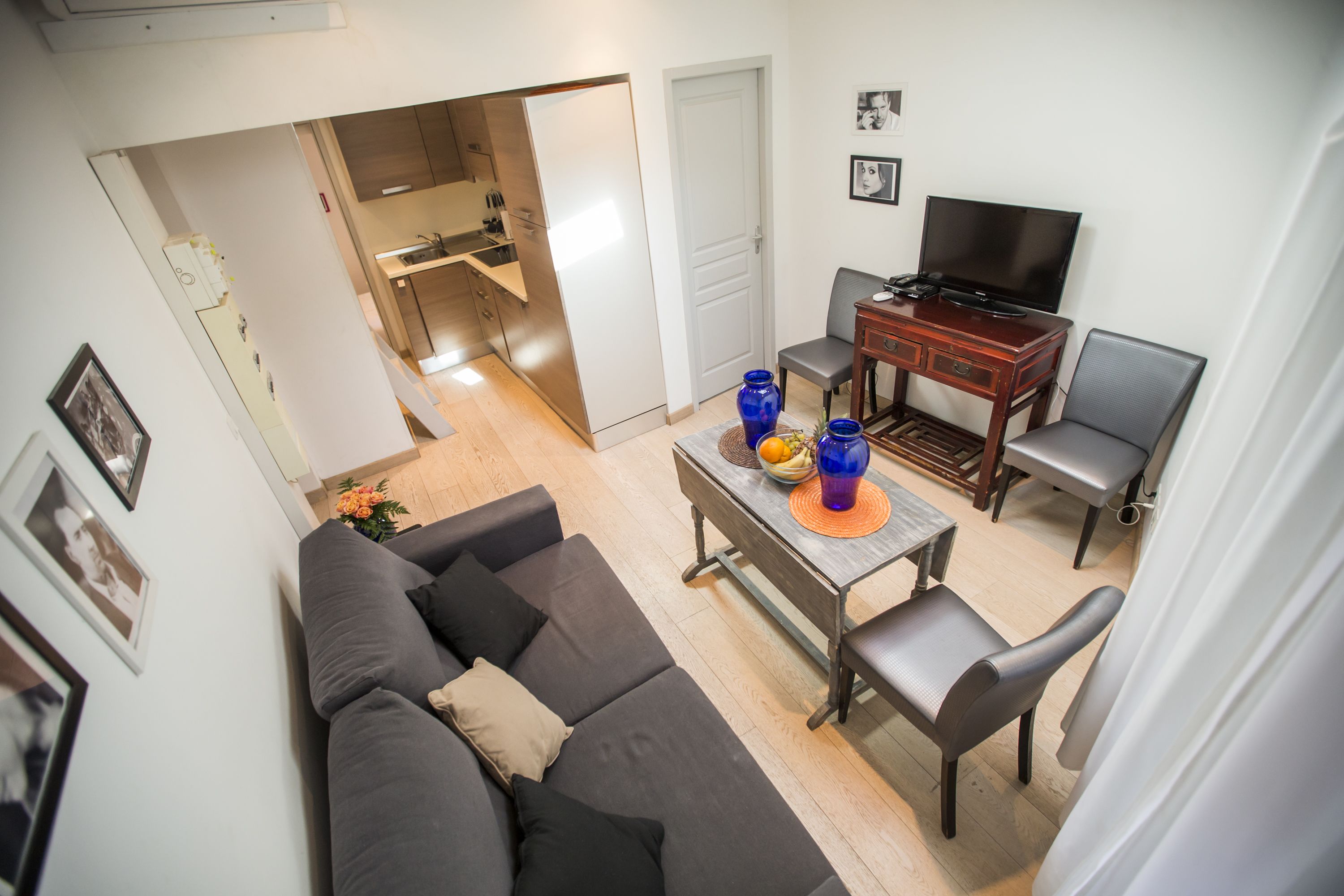 A modern living room with a sofa, a dining table with chairs, a TV, and a kitchen area in the background.