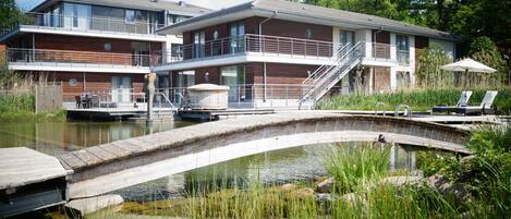 A modern two-story building with a wooden facade, a balcony, and a dock extending into a calm body of water.
