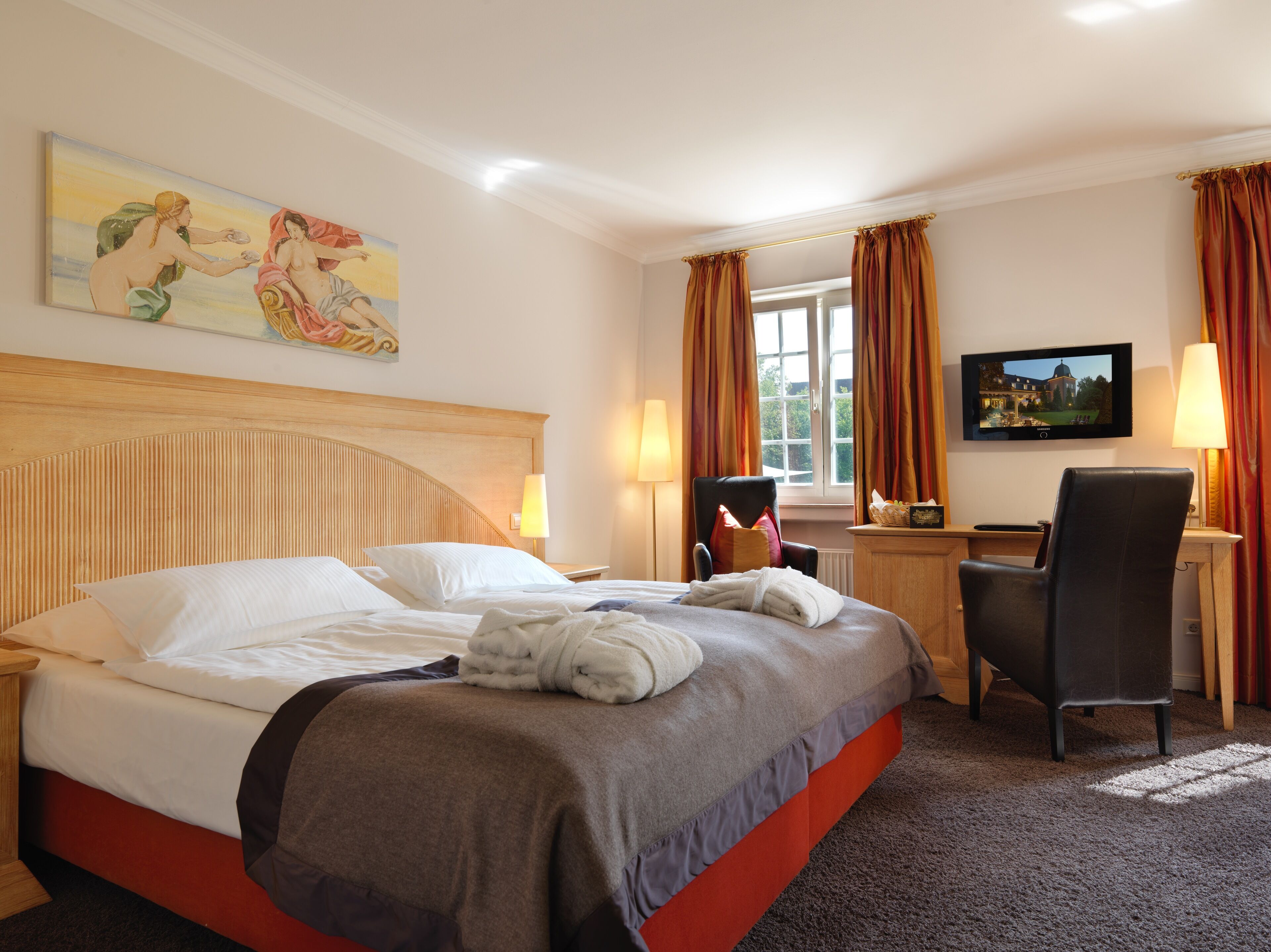 Una habitación de hotel con una cama grande, un escritorio, una silla, un televisor y un cuadro en la pared.