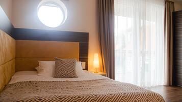 Ein Hotelzimmer mit einem großen Bett, einem runden Fenster, einem Nachttisch mit Lampe und transparenten Vorhängen.