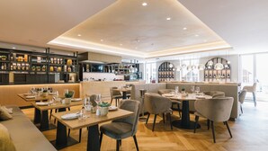 Een modern restaurant met houten vloeren, beklede zitplaatsen en een bar met flessen op de planken.