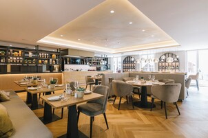 Un restaurante moderno con suelo de madera, asientos acolchados y una zona de bar con estantes llenos de botellas.