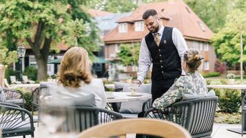 Ein Straßencafé mit Korbstühlen und Tischen, ein Kellner bedient einen Gast.