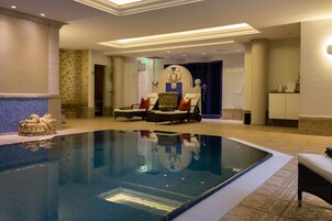 Una piscina con zona de descanso, una estatua y un muro decorativo.