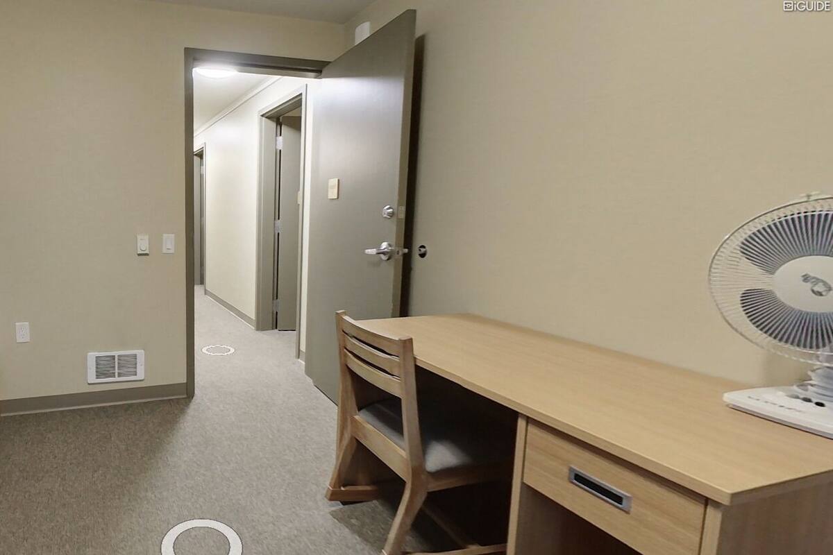 A room with a bunk bed, a desk, a chair, and a standing fan.