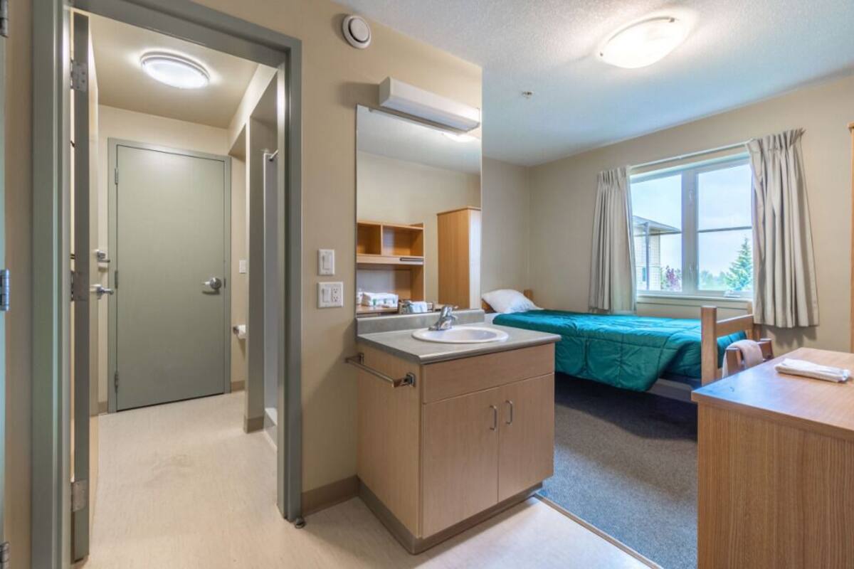 A hotel room with a bathroom, a bed, a desk, and a window with curtains.