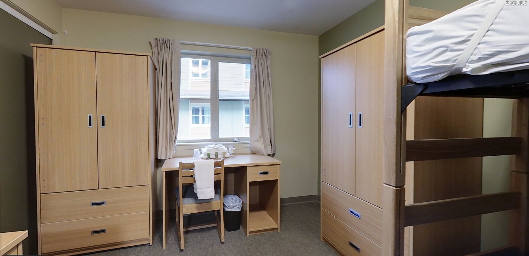 Een slaapkamer met een stapelbed, een bureau met stoel, en twee kledingkasten.