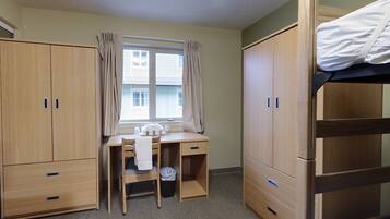 Een slaapkamer met een stapelbed, een bureau met stoel, en twee kledingkasten.