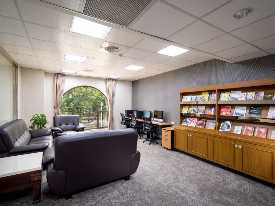 Escritório moderno com assentos de couro, área de trabalho, vários monitores de computador e uma estante com diversos livros.
