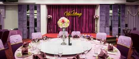 A round table set for a wedding reception with purple tablecloths, gold and purple napkins, and a floral centerpiece.