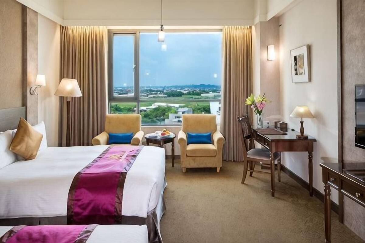 A hotel room with a large bed, two armchairs, a desk, and a view of the city.
