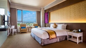 A hotel room with a large bed, a desk with a chair, a TV, and a view of the city. - Royal Chiayi Hotel (Chiayi City)
