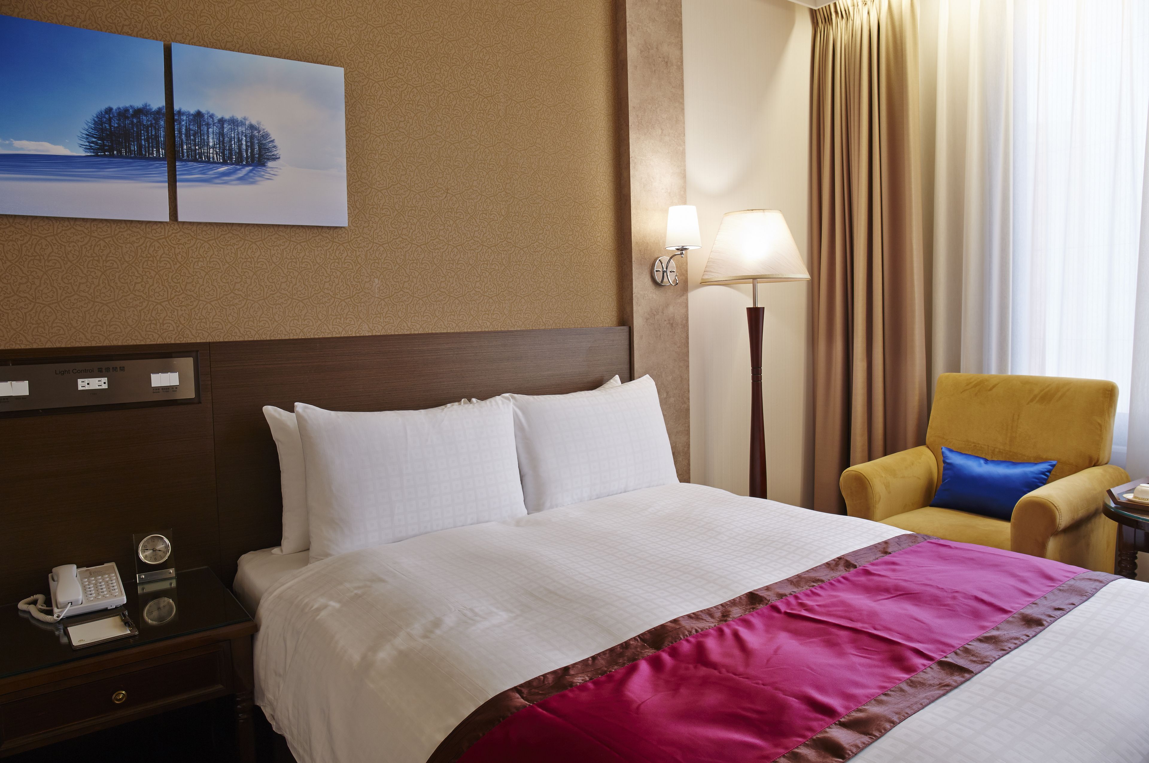 Une chambre d’hôtel avec un grand lit, une table de chevet avec un téléphone, une lampe et une chaise.