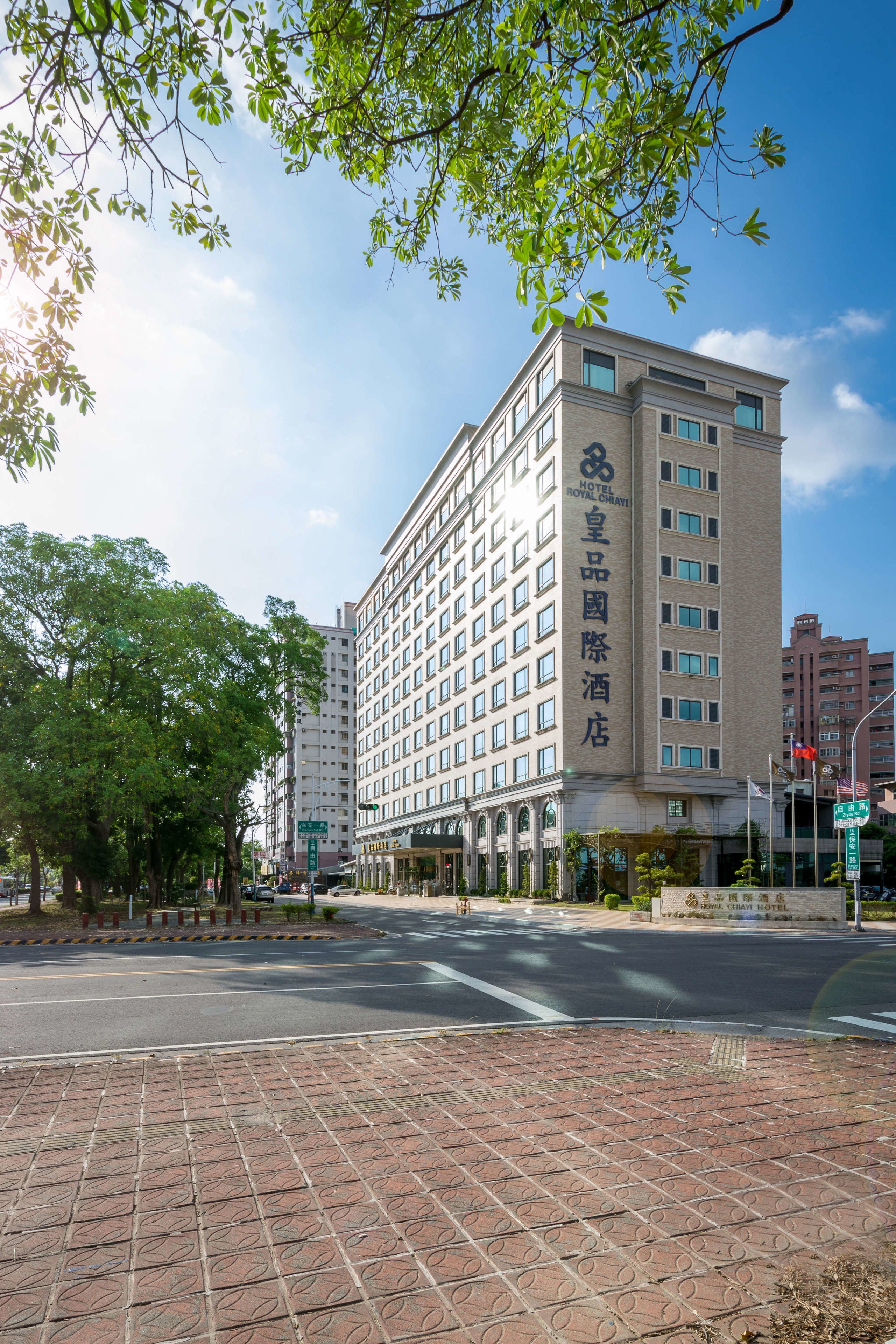 A multi-story hotel with a prominent sign, a paved sidewalk, and trees in the foreground.