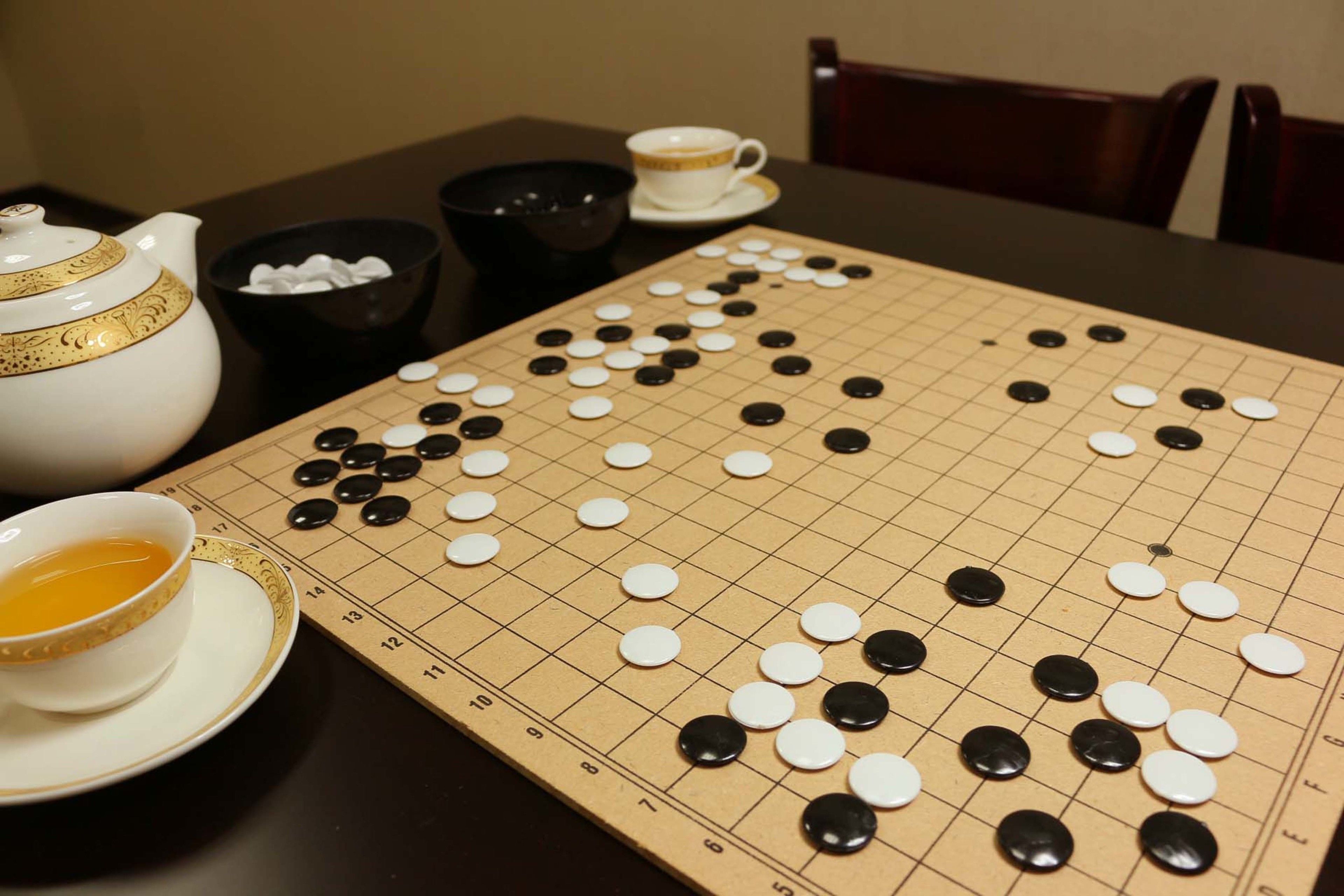 A Go board with pieces in play, a teapot, a cup, and a bowl on a table.