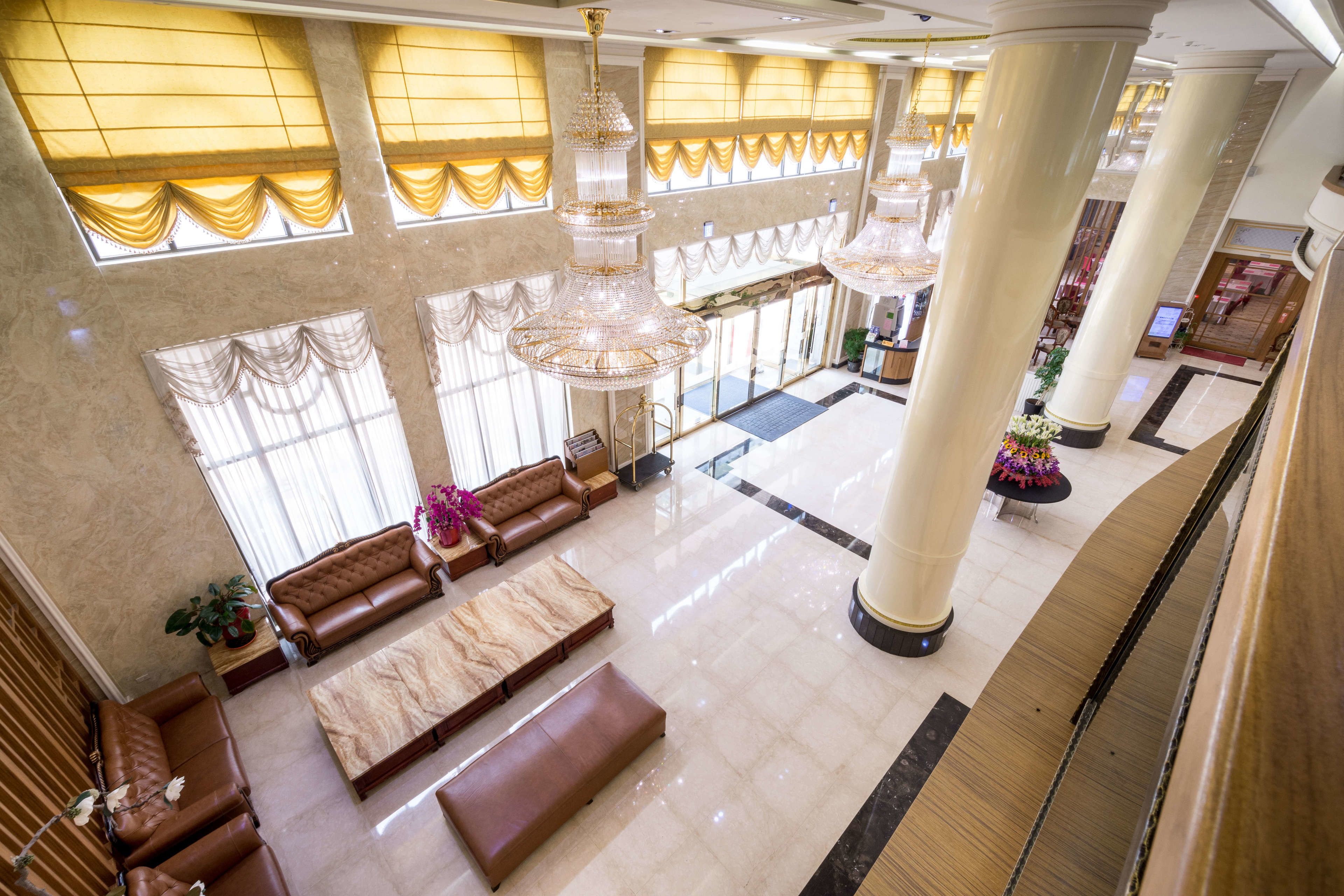 A spacious lobby with high ceilings, large chandeliers, and a grand staircase.