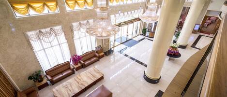 A spacious lobby with high ceilings, large chandeliers, and a grand staircase.