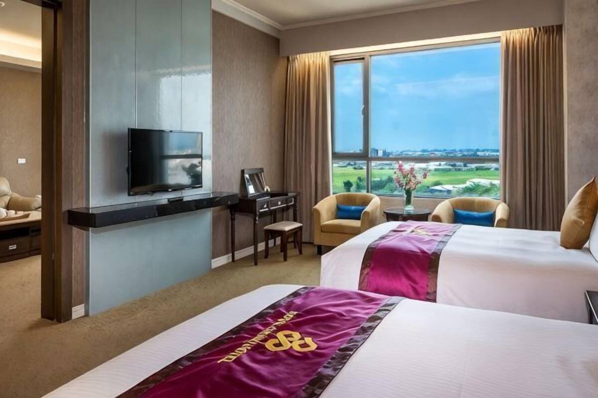 A hotel room with two beds, a desk, a TV, and a view of the landscape.