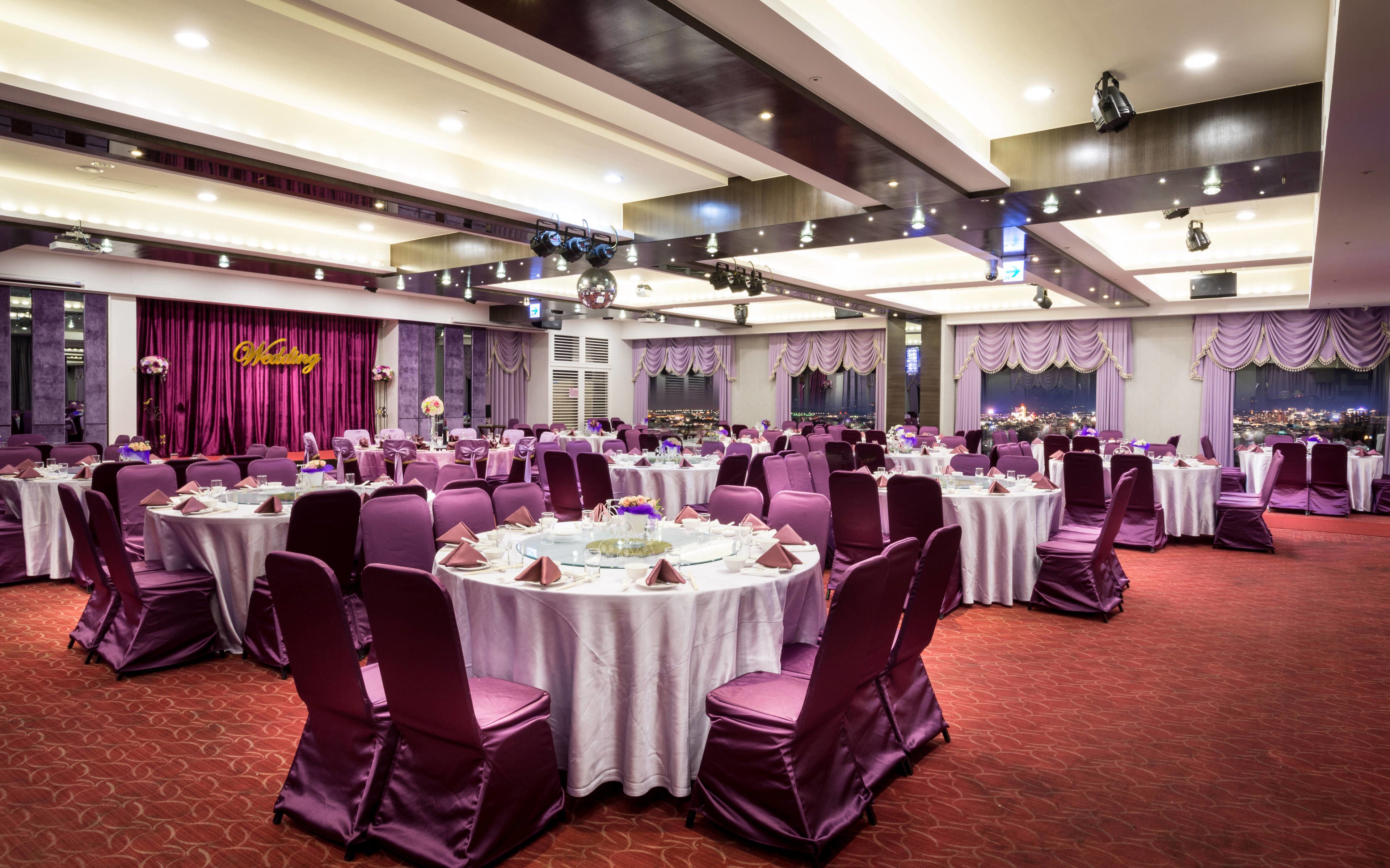 A banquet hall with round tables, purple chairs, and a red carpet.