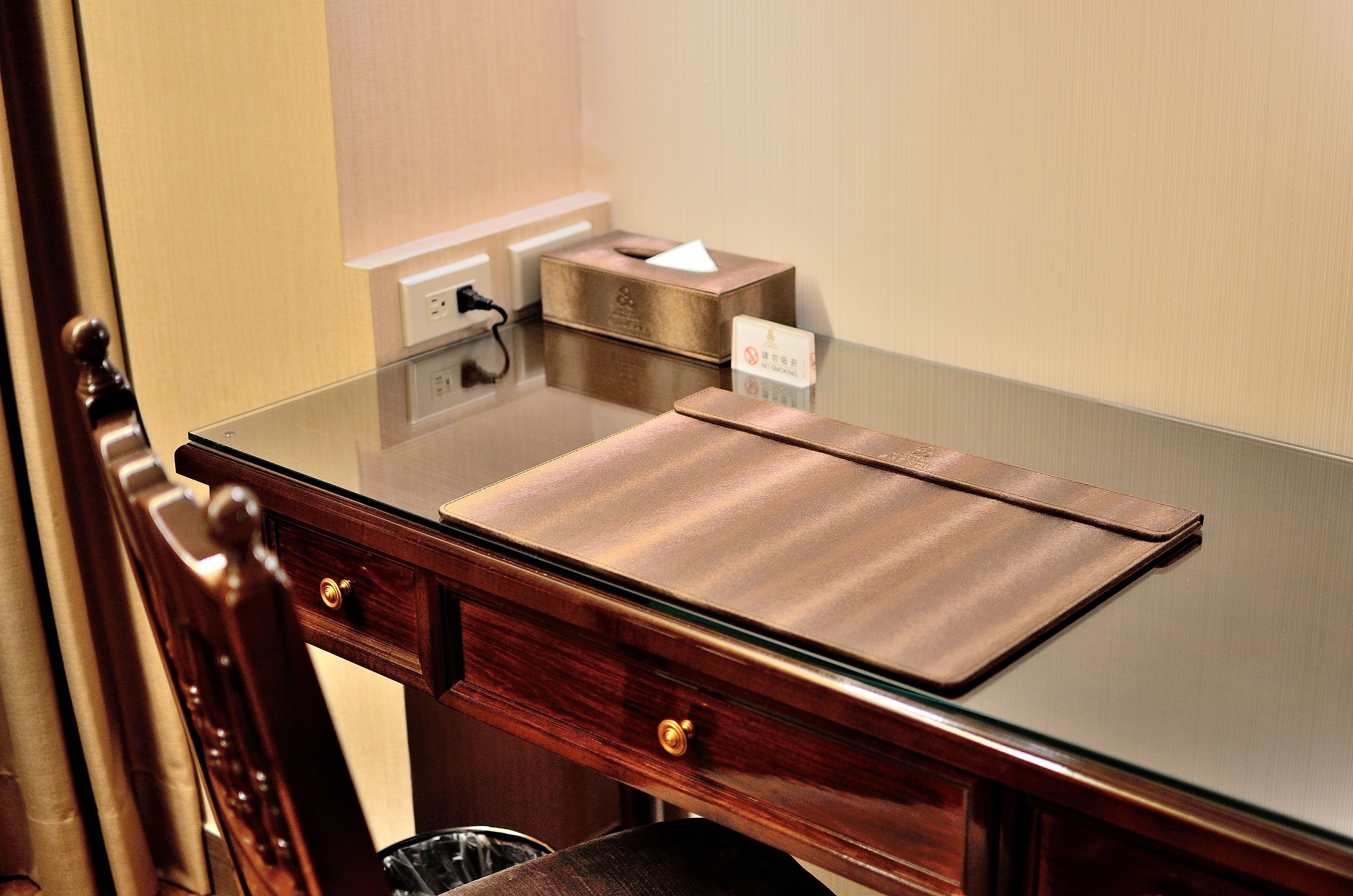 A wooden desk with a glass top, a tissue box, and a sign with a prohibition symbol.
