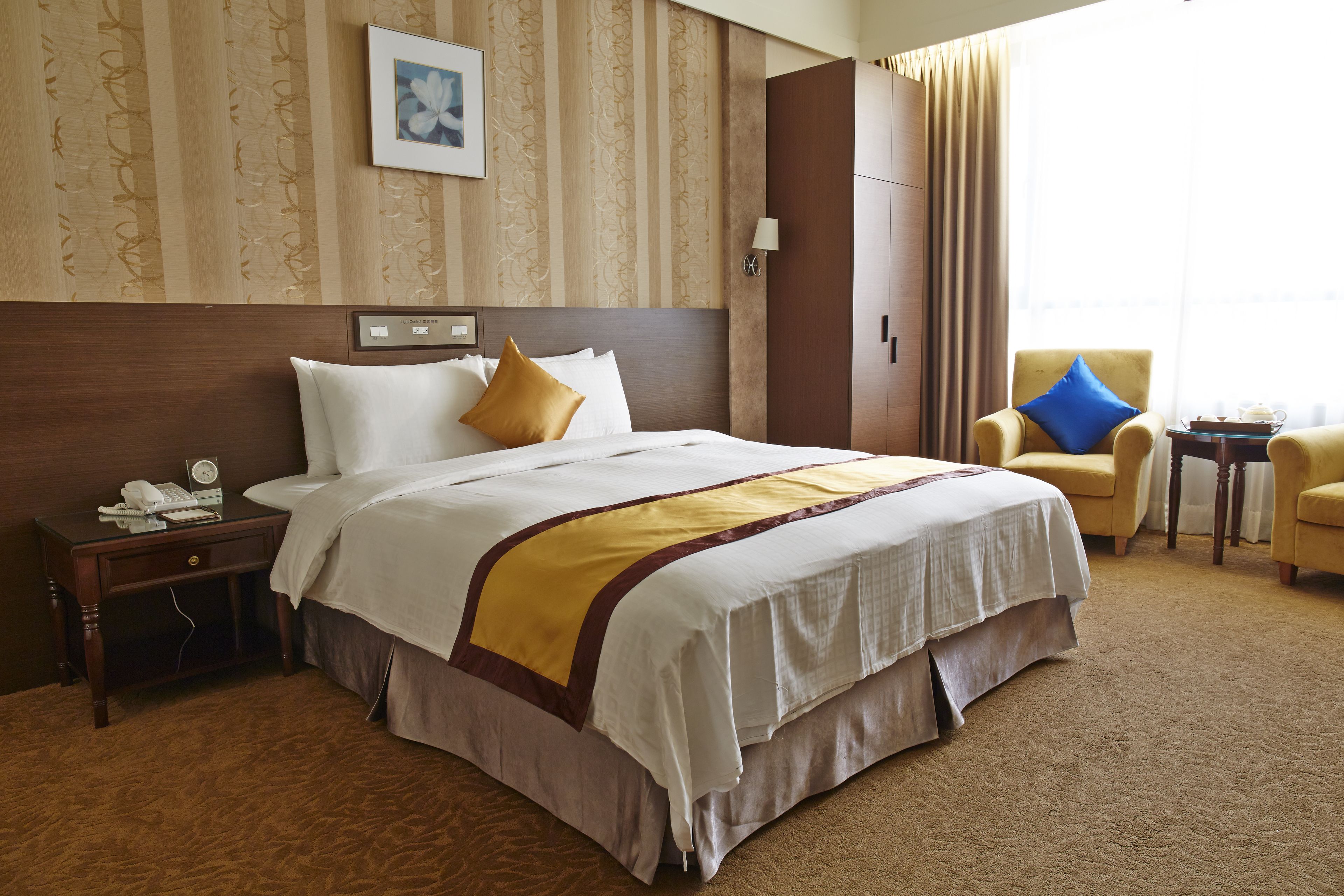 A hotel room with a large bed, a nightstand with a telephone, a chair, and a small table with a tray.