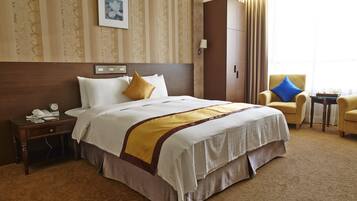 A hotel room with a large bed, a nightstand with a telephone, a chair, and a small table with a tray.