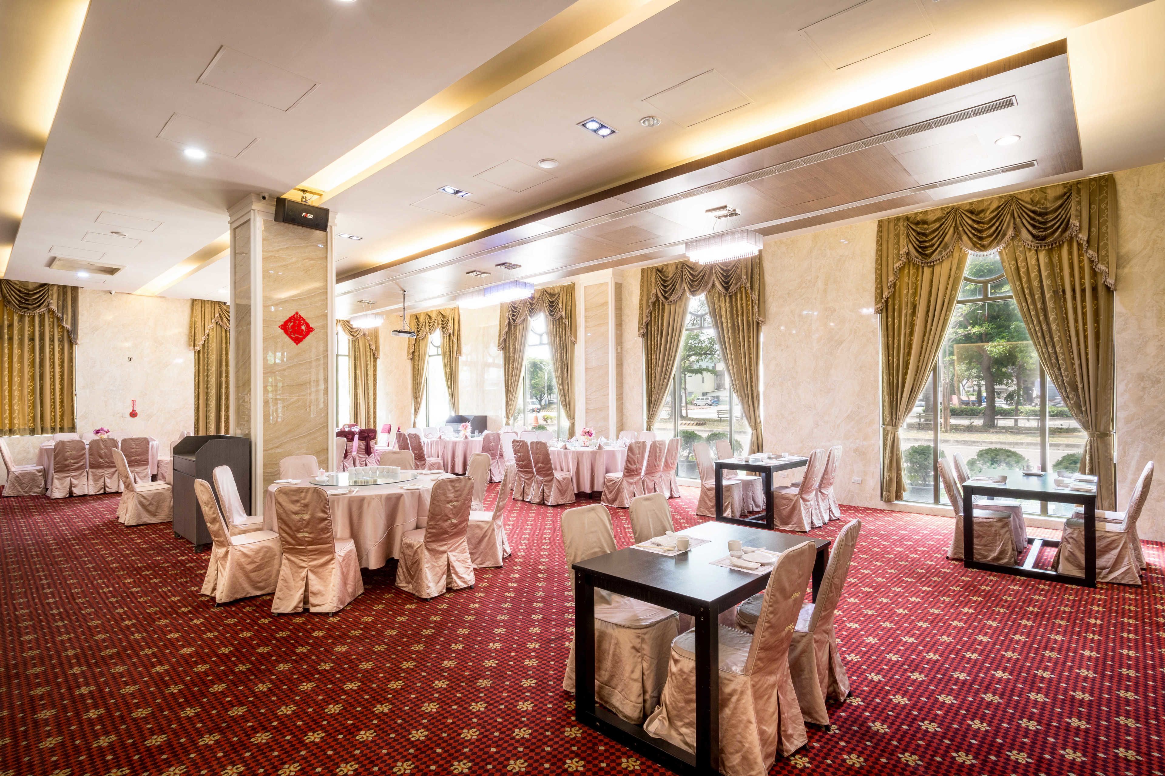 A banquet hall with round tables, chairs, and a red carpeted floor.