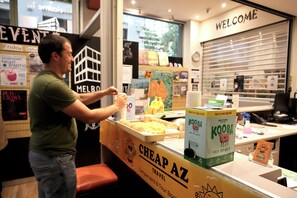 Un homme se tient derrière un comptoir, et une pancarte indique : « VOYAGES À PETITS PRIX ».